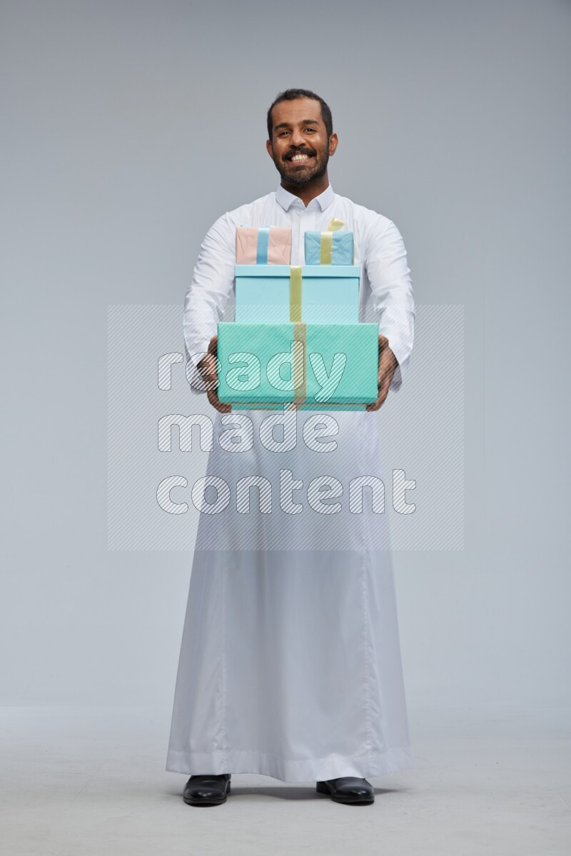Saudi man Wearing thob standing holding gift box on Gray background