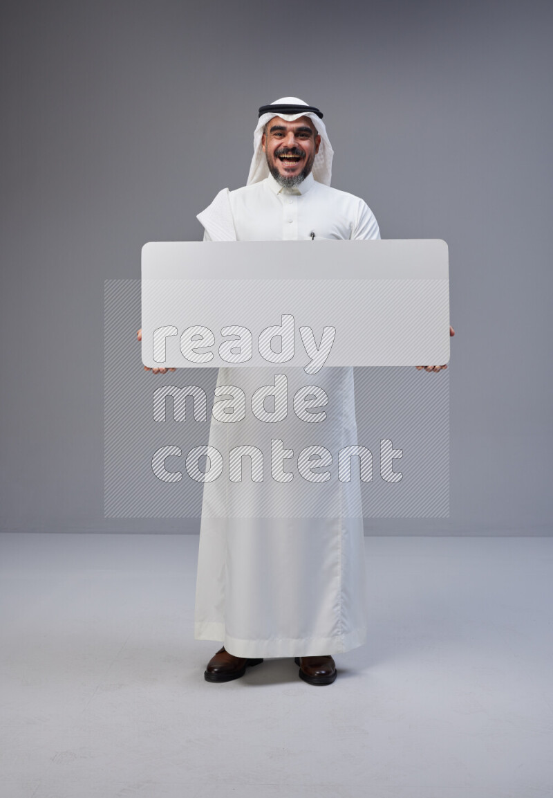 Saudi man Wearing Thob and white Shomag standing holding board on Gray background