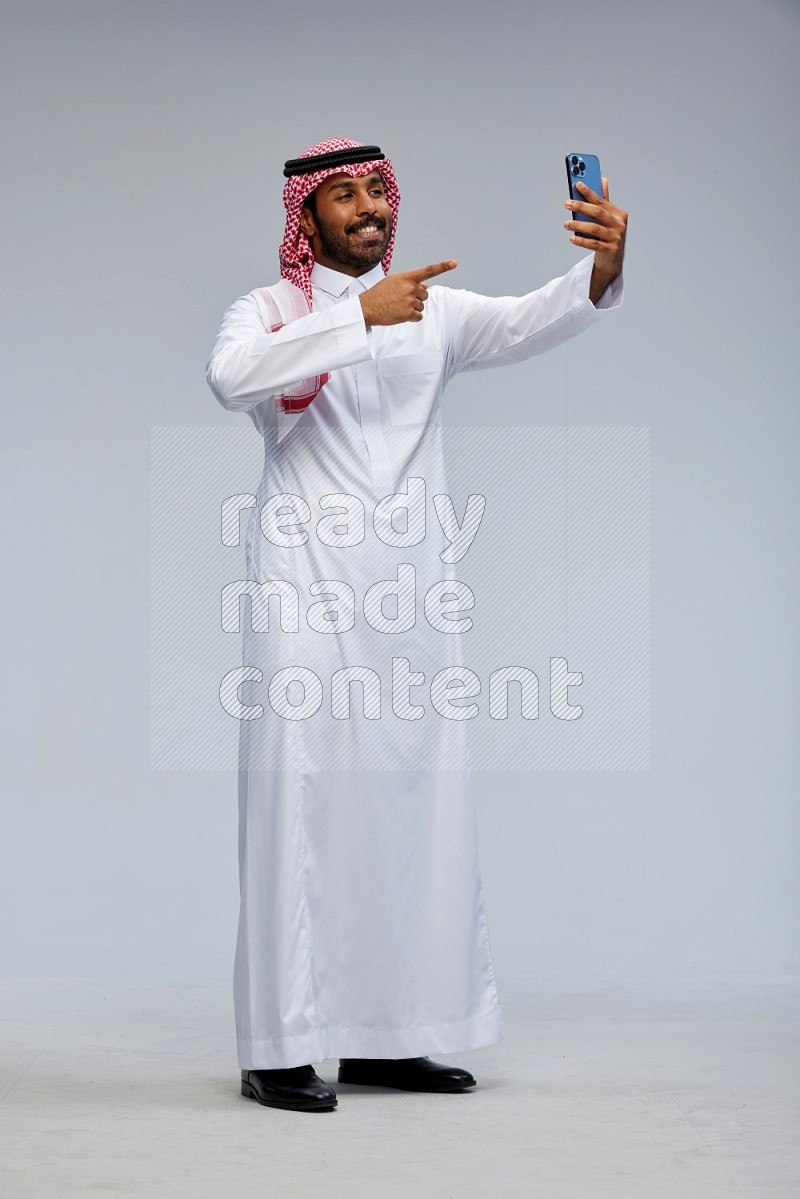 Saudi man Wearing Thob and shomag standing taking selfie on Gray background