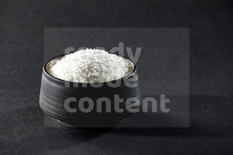 A black pottery bowl full of desiccated coconut on a black background in different angles