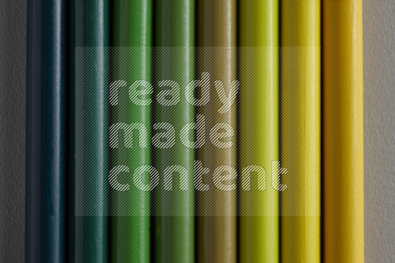 A collection of sharpened colored pencils arranged showcasing a gradient of yellow and green hues on grey background