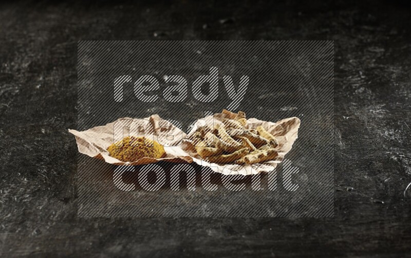 أصابع الكركم المجففة وبودرة الكركم في قطع من الورق على خلفية سوداء