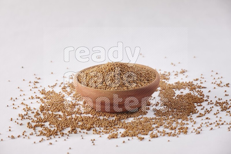 A wooden bowl full of mustard seeds and more seeds spread on a white flooring