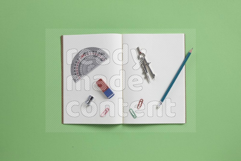A blank open notebook with school supplies on green background (Back to school)