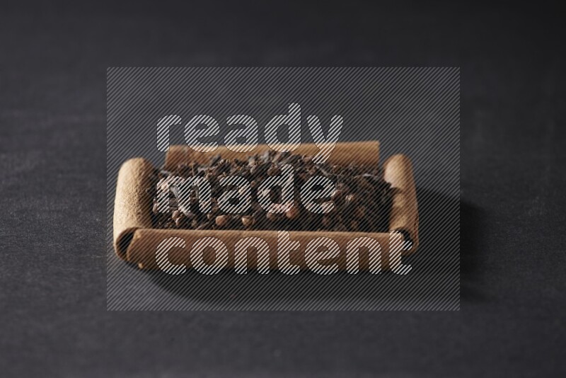 أربعة من أعواد القرفة مكونة شكل مربع بداخلها حبوب قرنفل علي خلفية سوداء