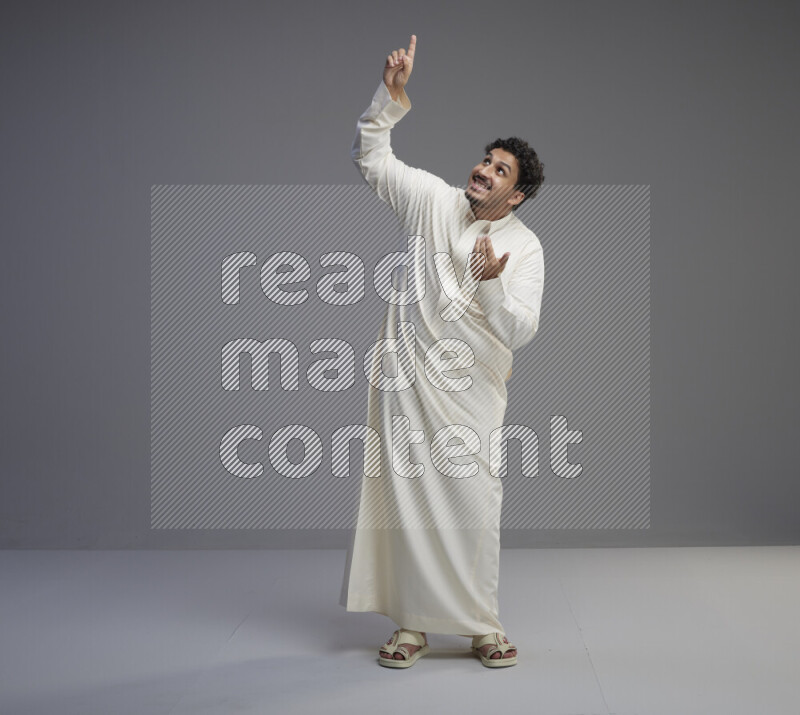 A Saudi man standing wearing thob interacting with the camera on gray background