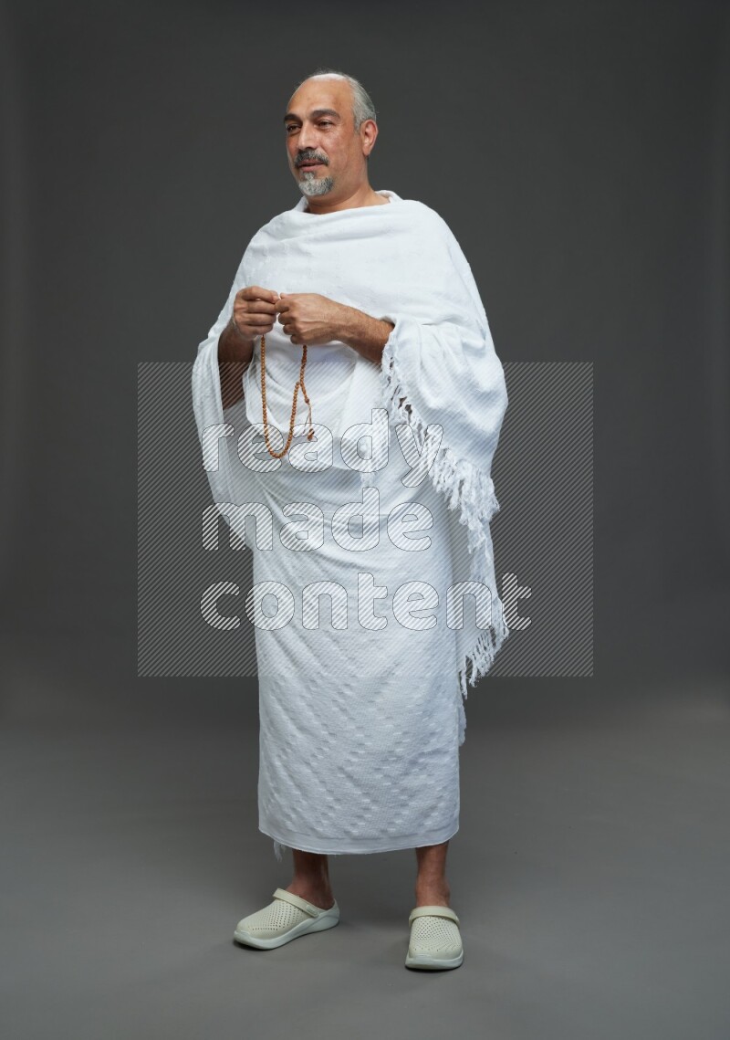 A man wearing Ehram Standing holding rosary on gray background
