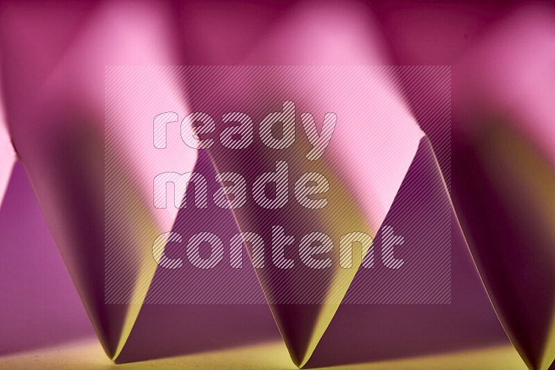 A close-up abstract image showing sharp geometric paper folds in pink gradients and warm tones