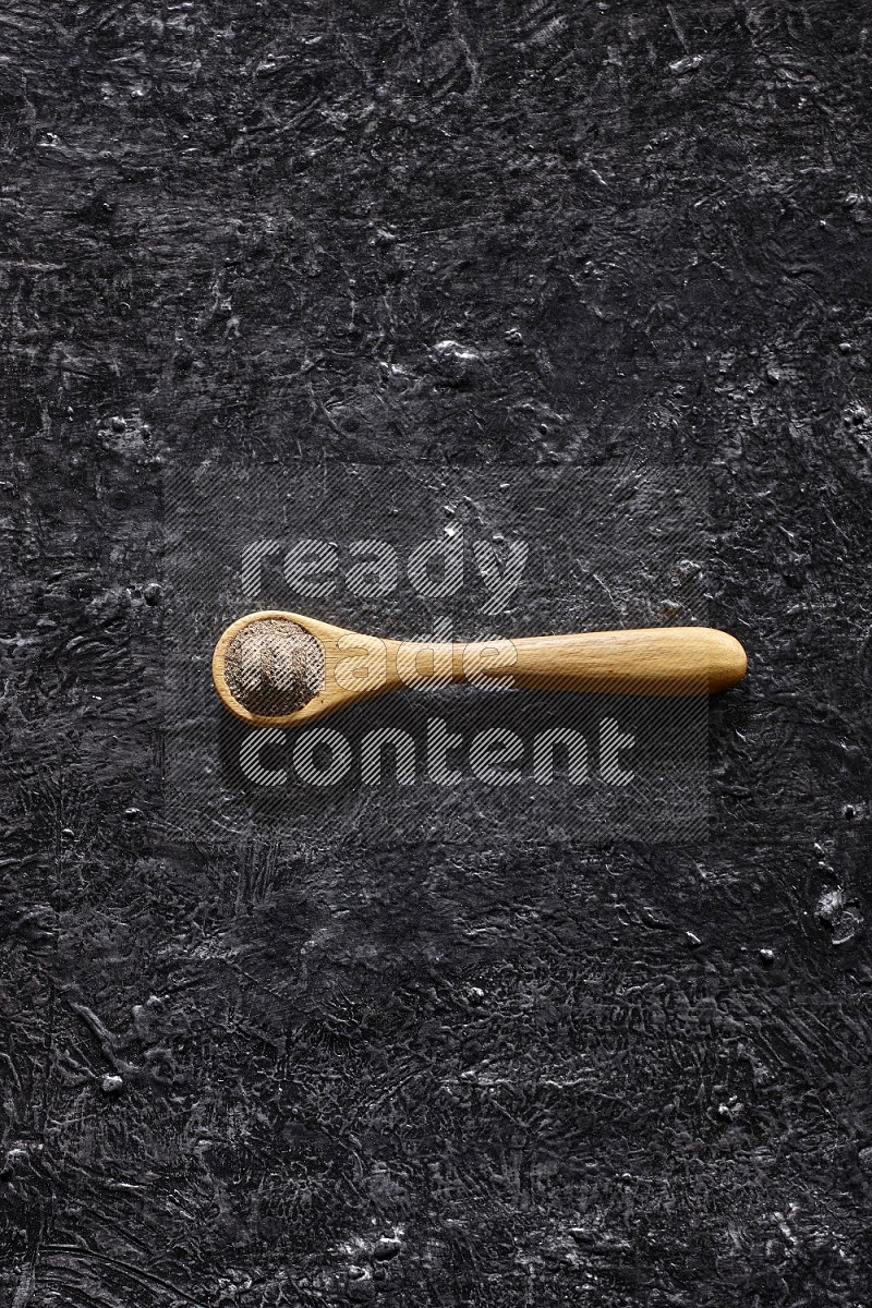 حبوب الفلفل الأسود في ملعقة خشبية علي خلفية سوداء