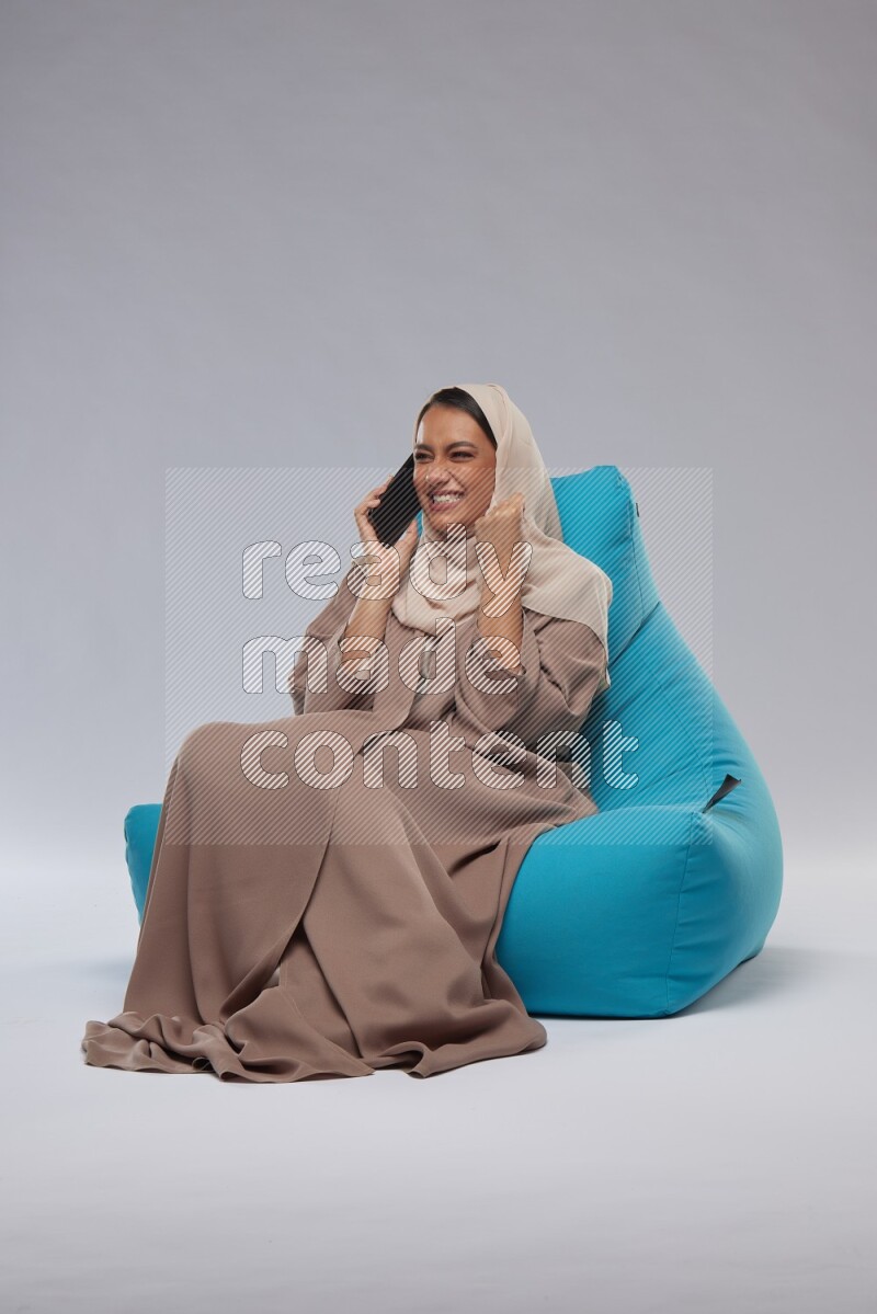 A Saudi woman sitting on a blue beanbag and working on laptop