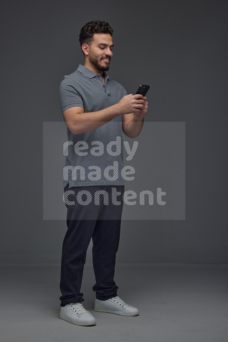 A man wearing casual standing and using his phone eye level on a gray background
