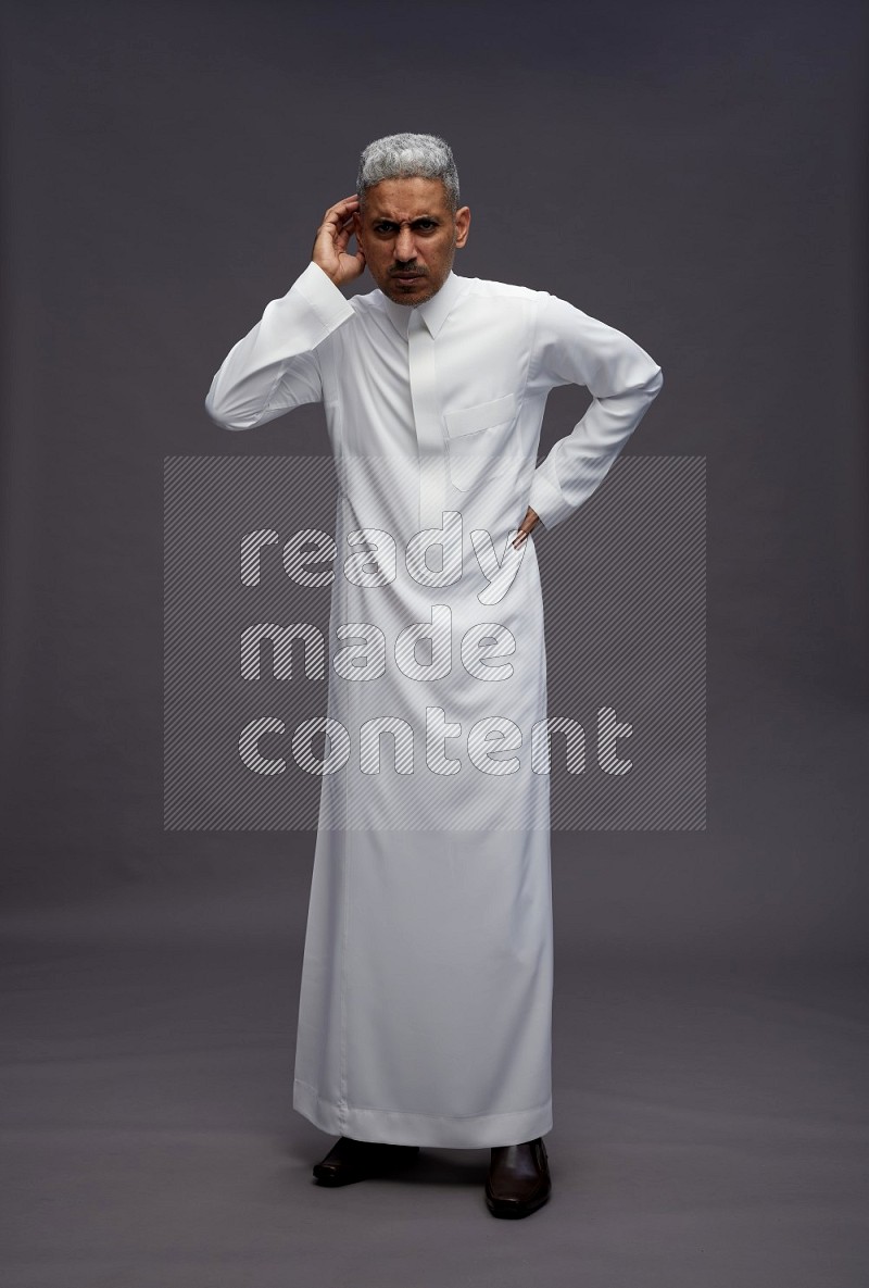 Saudi man wearing thob standing interacting with the camera on gray background