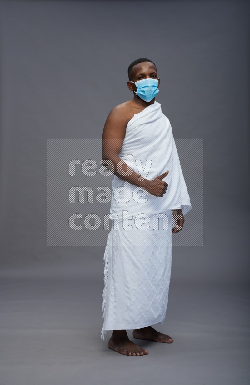 A man wearing Ehram with face mask Standing Interacting with the camera on gray background