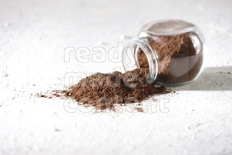 A flipped glass spice jar full of cloves powder and powder came out of it on textured white flooring