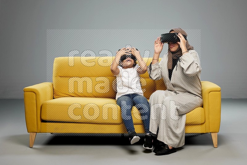 A girl and her mother sitting playing with VR on gray background