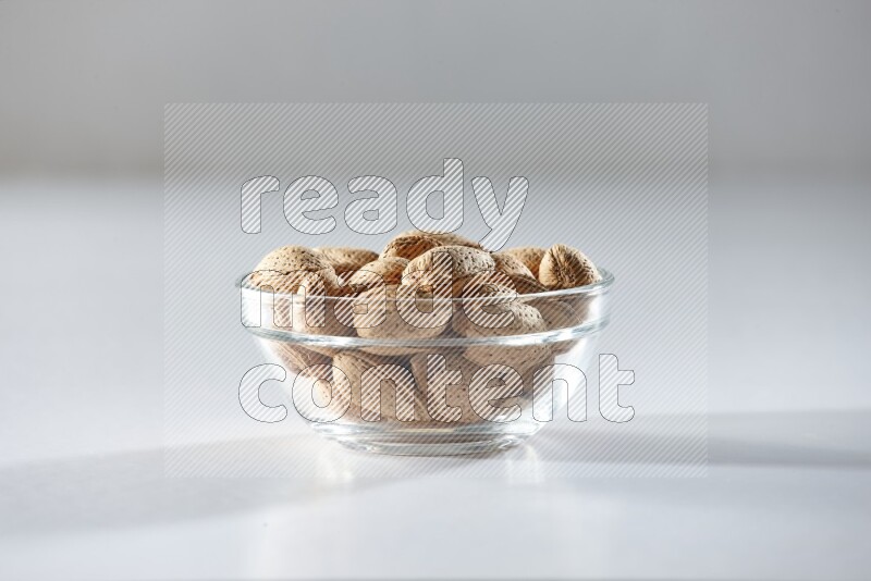 A glass bowl full of almonds on a white background in different angles
