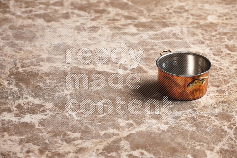 A small copper pot on beige marble background