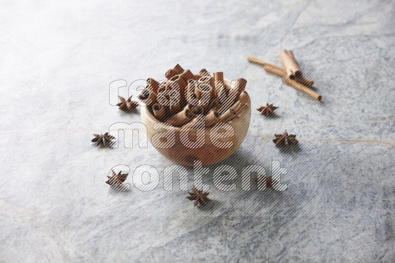 wooden bowl full of cinnamon sticks surrounded by star anis on marble background in different angles