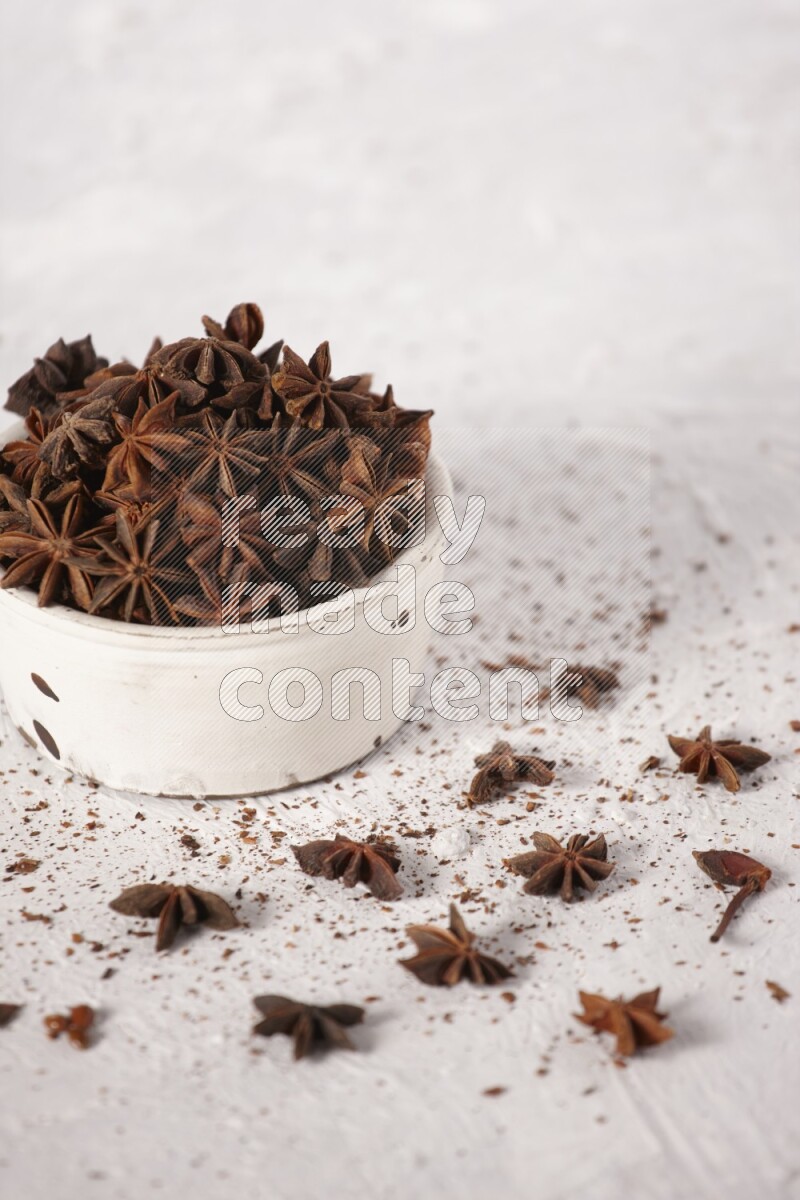 Star Anise in a white bowl and more of it sprinkled on white background