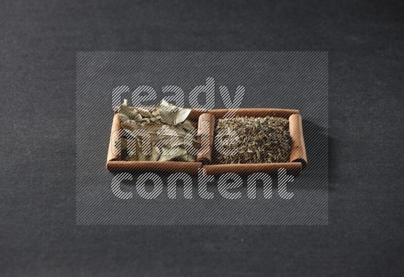 مربعان من أعواد القرفة ممتلئان بحبوب الكمون وأوراق الغار علي خلفية سوداء