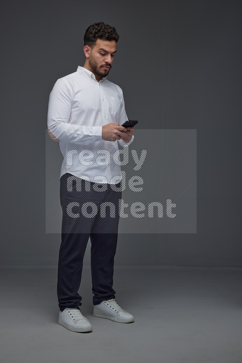 A man wearing smart casual standing and using his phone eye level on a gray background