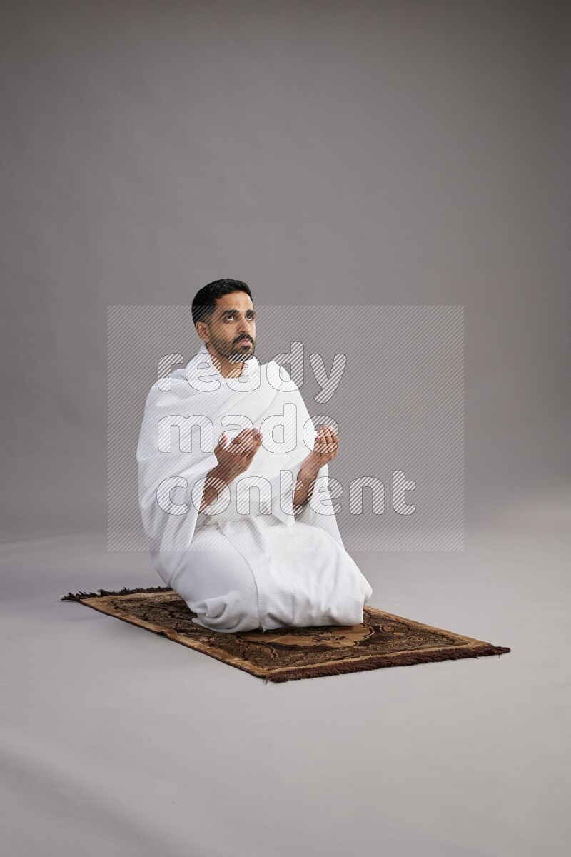 A man wearing Ehram performing dua'a on gray background