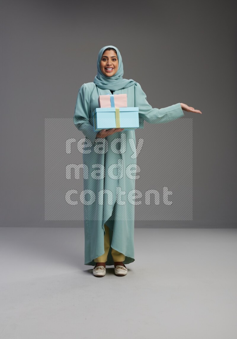 Saudi Woman wearing Abaya standing holding gift box on Gray background