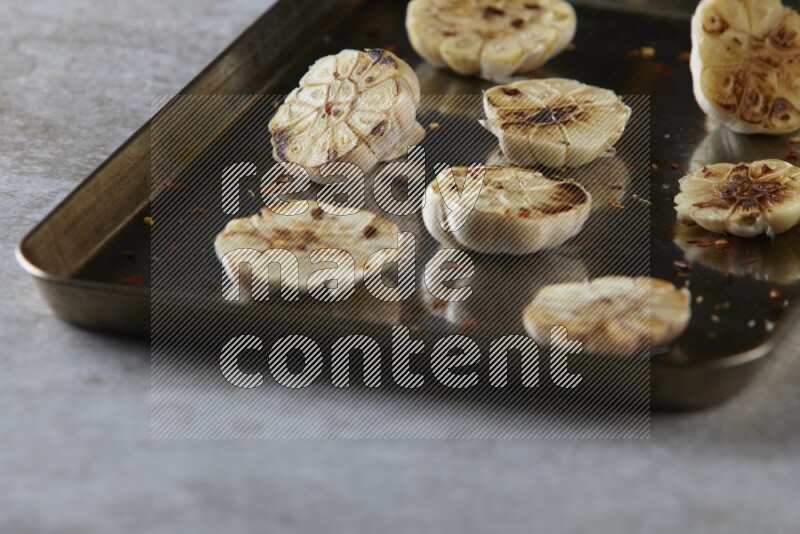 half's roasted garlic in a stainless tray on a grey textured countertop
