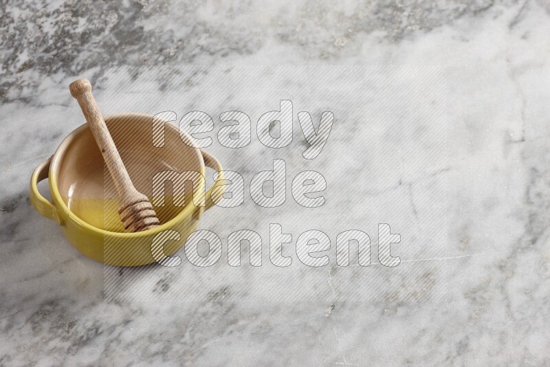 Multicolored pottery bowl with wooden honey dipper in it on grey marble background