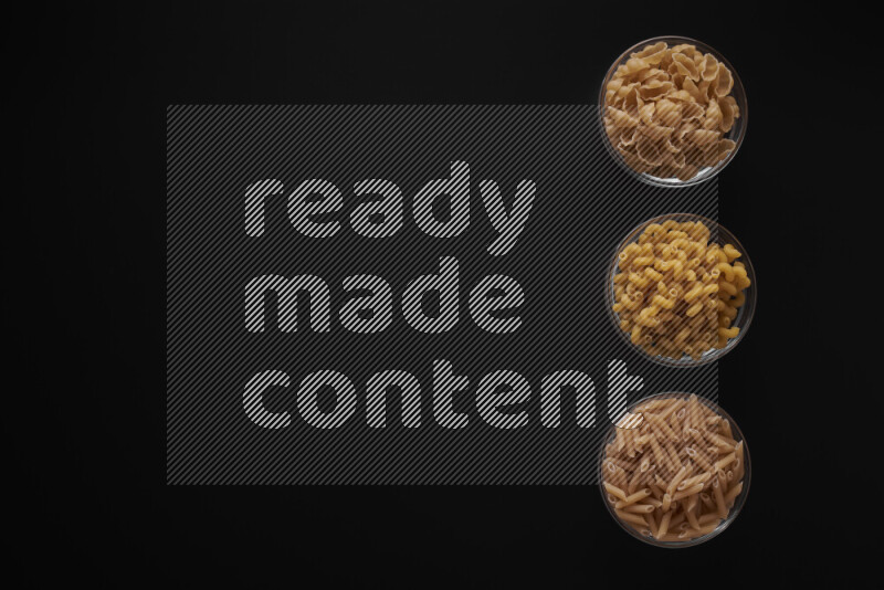 Different pasta types in 3 glass bowls on black background