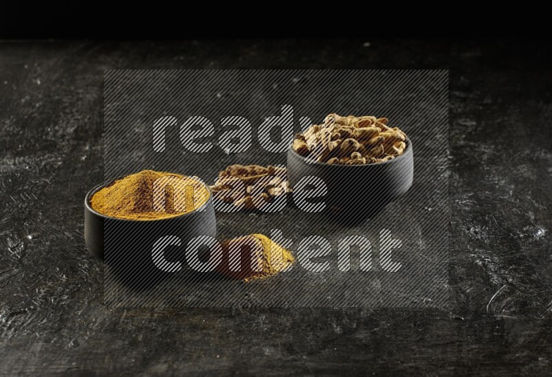 وعاءان من الفخار باللون الأسود، أحدهما ممتلئ ببودرة الكركم والآخر ممتلئ بأصابع كاملة من الكركم المجفف على خلفية سوداء