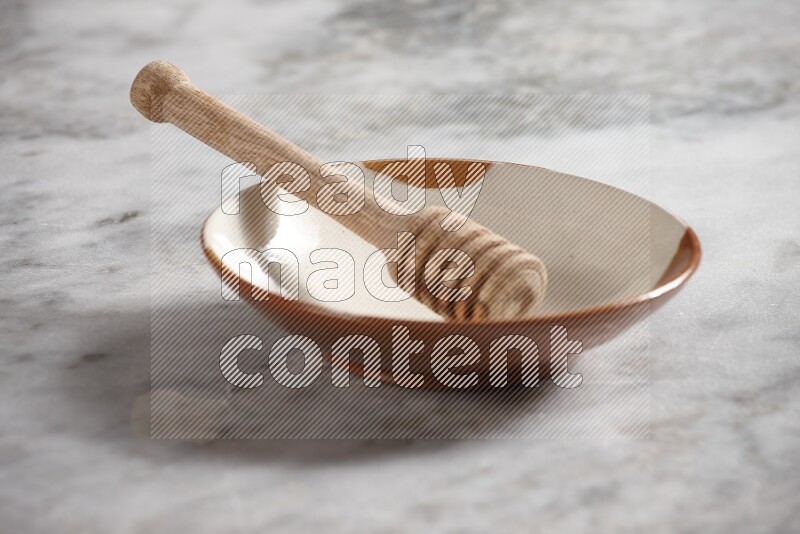 Multicolored pottery plate with wooden honey dipper in it on grey marble background