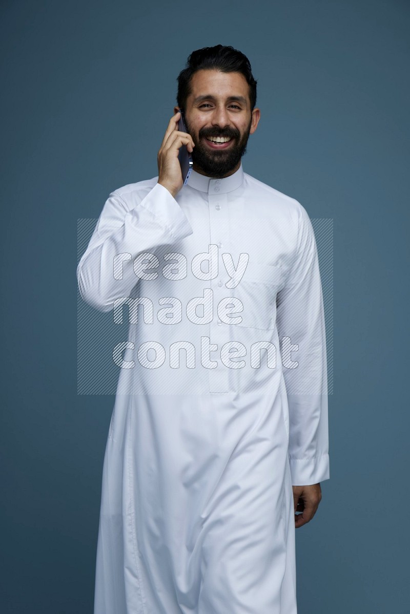 A man having a call on a blue background wearing Saudi Thob