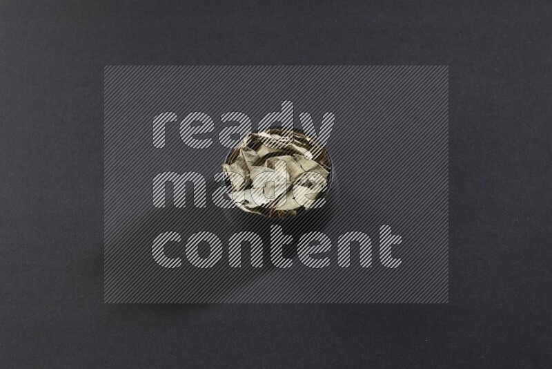 وعاء فخاري أسود ممتلئ بأوراق الغار المجففة على أرضية سوداء