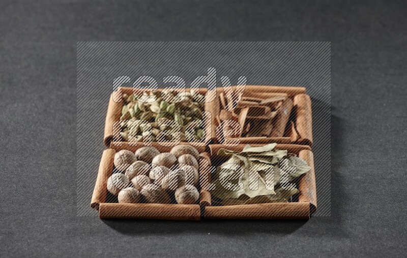 4 مربعات من عيدان القرفة ممتلئة بقطع القرفة وحبوب الهيل وأوراق الغار وجوزة الطيب على أرضية سوداء