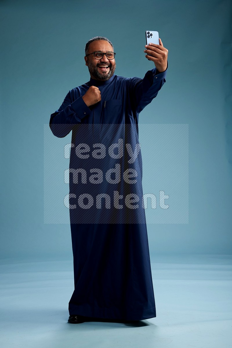 Saudi Man without shimag Standing taking selfie on blue background