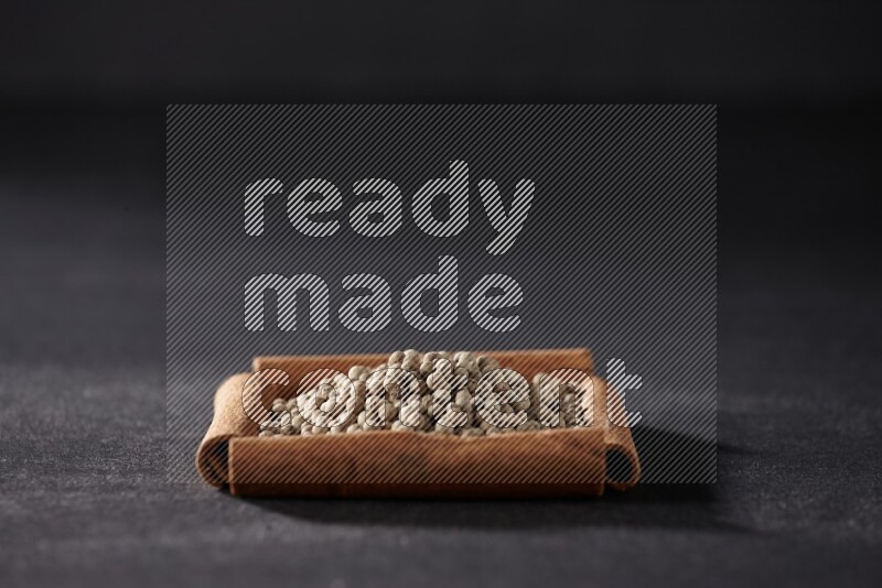 A single square of cinnamon sticks full of white pepper on black flooring