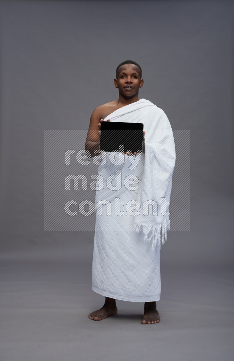 A man wearing Ehram Standing showing tablet to camera on gray background