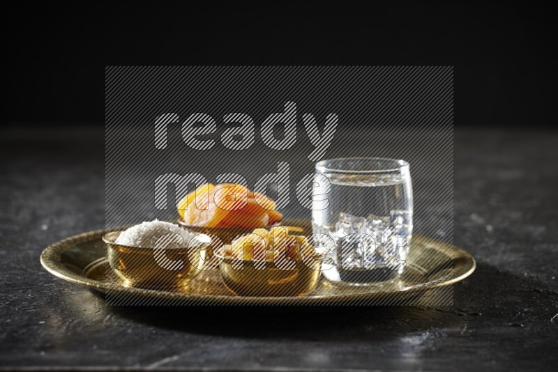 Dried fruits in metal bowls with water on a tray in dark setup