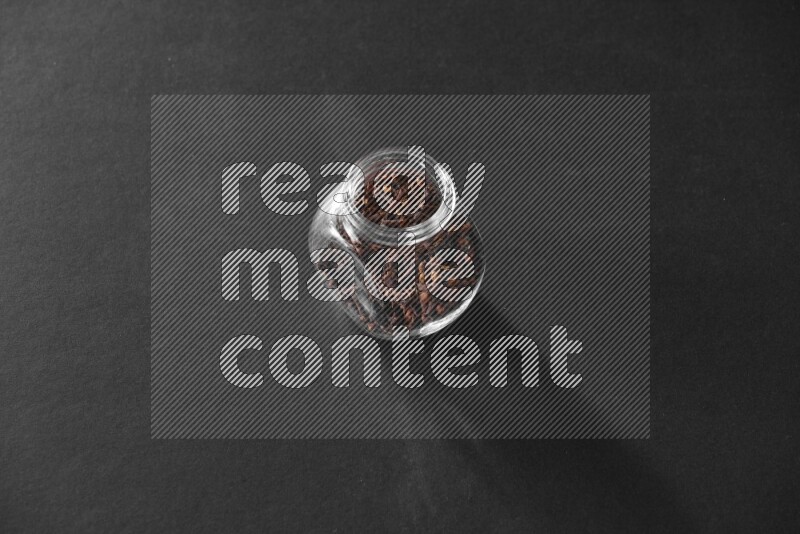 A glass spice jar full of cloves on black flooring