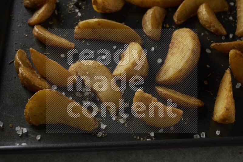 wedges potato in a black stainless steel rectangle tray on grey textured counter top