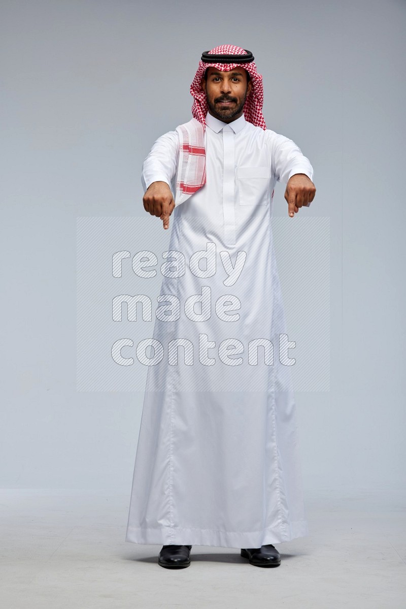 Saudi man Wearing Thob and shomag standing interacting with the camera on Gray background