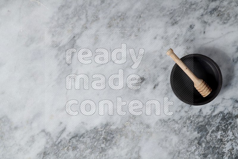 Black Pottery Oven Plate with wooden honey handle in it, on grey marble flooring, Top View