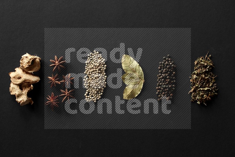 Ginger, star anise, white pepper, laurel bay leaves, black pepper and basil lined on a black background