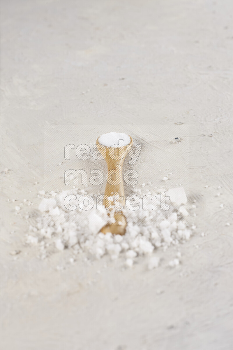 A wooden spoon full of white salt on white background