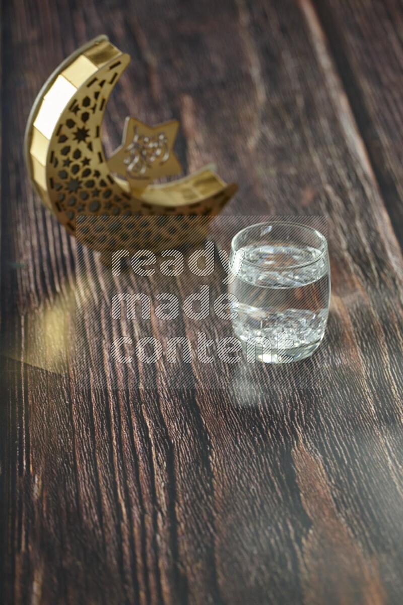 A wooden golden crescent lantern with different drinks, dates, nuts, prayer beads and quran on brown wooden background