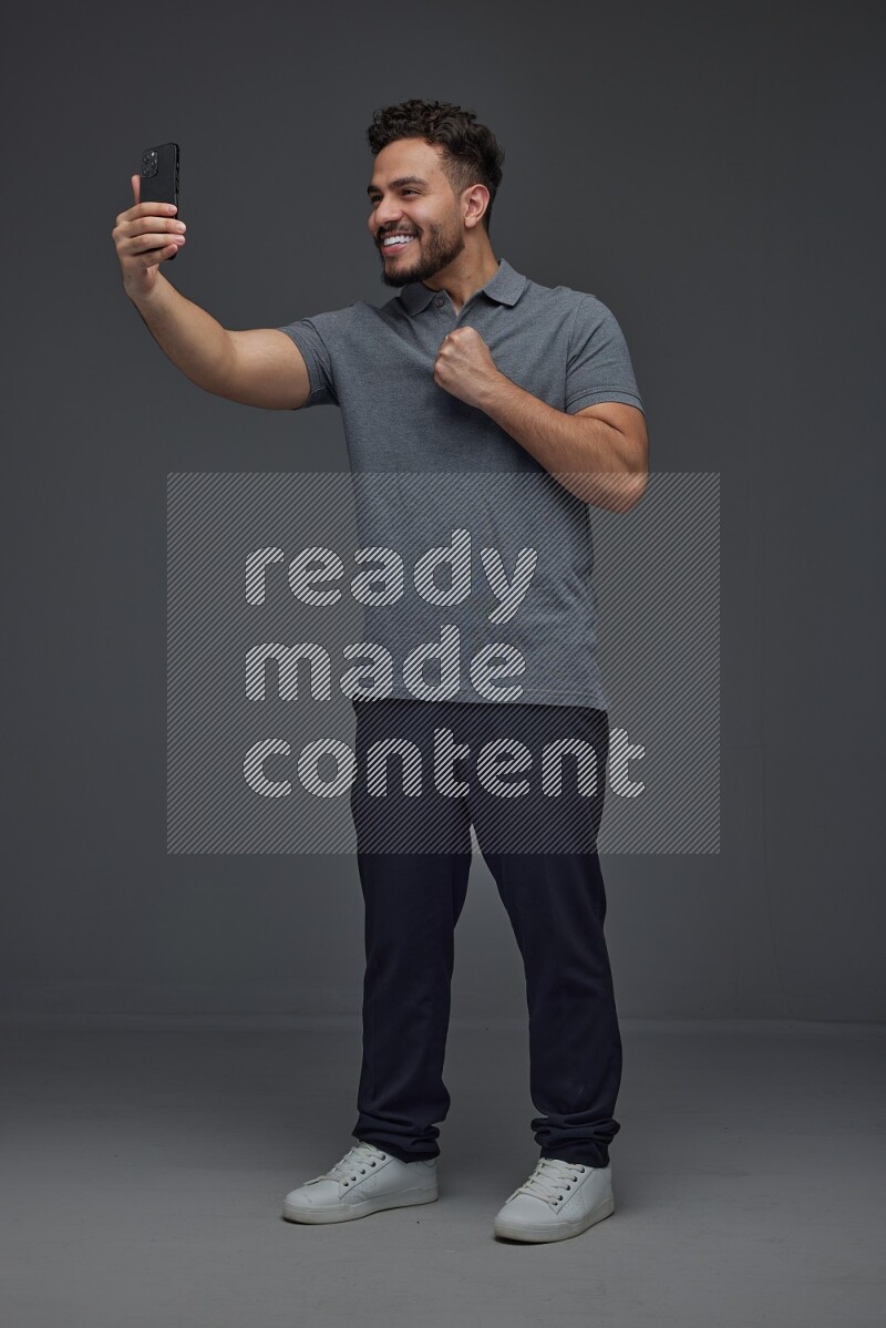 A man wearing casual and taking selfie with his phone different angles eye level on a gray background