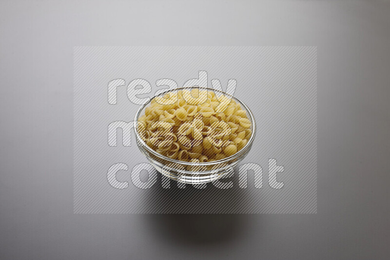 Shells pasta in a glass bowl on grey background