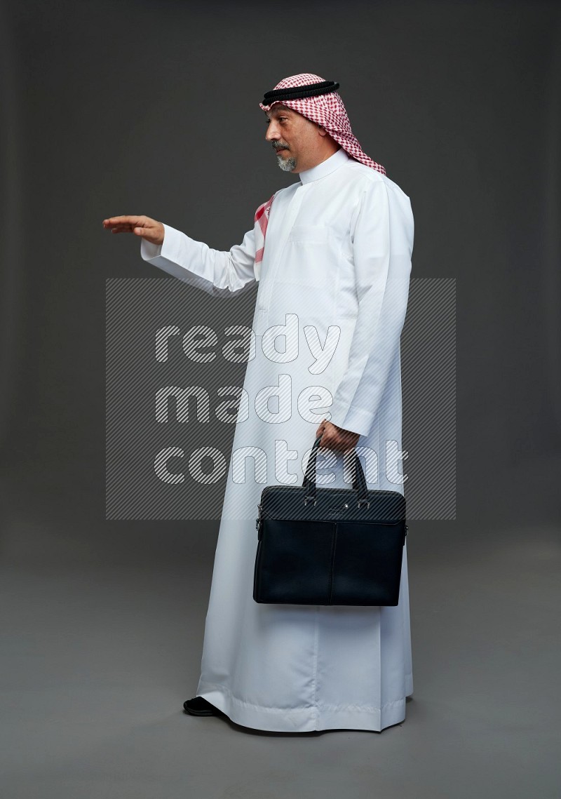 Saudi man with shomag Standing holding bag on gray background