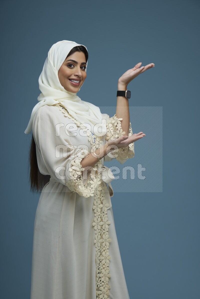 A Saudi woman pointing in a blue background wearing an off-white Abaya Hijab